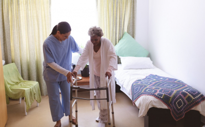  Front view of mixed race female nurse helping senior mixed race female patient to stand with walker at nursing home