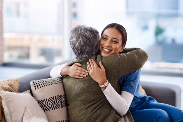 smiling caregiver hugging a senior woman on a couch